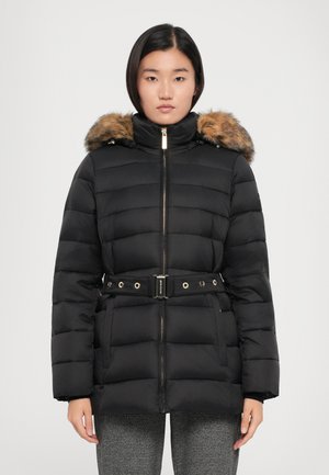 Giacca a puffo nera con cappuccio foderato in pelliccia, vita con cintura, accessori in oro e texture trapuntata. Abbinata a pantaloni grigi a fantasia.