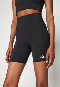 Pantaloni sportivi neri a vita alta realizzati in tessuto elasticizzato, con logo a tre strisce bianche a contrasto sulla gamba e cuciture lisce.