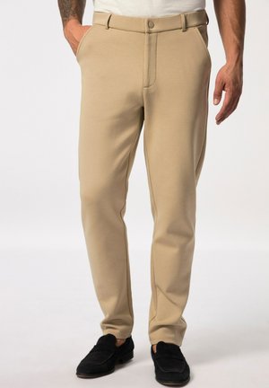 Beige, taillierte Hose mit glatter Textur, mit einem Knopfverschluss und seitlichen Taschen, kombiniert mit schwarzen Slippern.