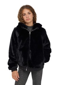 Hoodie in pelliccia sintetica nera con zip frontale, cappuccio e polsini a costine. Il modello indossa un top grigio luccicante e leggings lucidi. Tessuto morbido, fit ampio.