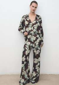 Blusa de mangas largas con estampado floral y pantalones de pierna ancha a juego en marrón oscuro con flores verdes y crema, confeccionados en tela ligera.