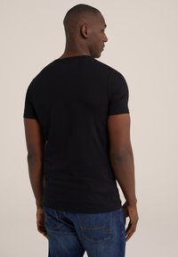 Zwart T-shirt met korte mouwen, gemaakt van katoen, slim fit ontwerp, ronde hals, gladde textuur. Gedragen met blauwe spijkerbroek.