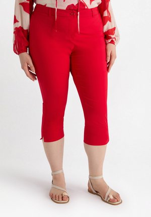 Pantalones cortos rojos con un diseño ajustado, textura suave y aberturas laterales en el dobladillo, combinados con sandalias planas beige.