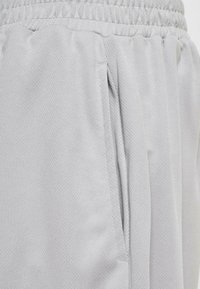 Lys grå sportshorts lavet af tekstureret stof med elastisk talje og sidelommer. Designet er løstsiddende og åndbart.