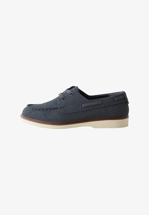 Dunkelblauer lässiger Bootsschuh mit weißer Sohle, Schnürung vorne, Mokassinnaht und einem Lederstreifen um die Ferse und Seiten.
