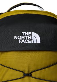 Black and yellow backpack featuring a textured surface, logo with white embroidery, and adjustable elastic cord on the front.