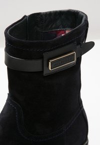 Svart mocka ankelboot med ett slätt läderrem och en spänne i guldton. Kontrastsydd framhäver designens detaljer.