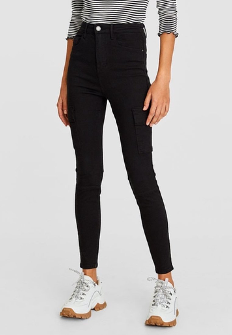 Jeans cargo de cintura alta en negro con un corte ajustado, que cuentan con bolsillos laterales y una textura suave, combinados con zapatillas blancas y marrones.