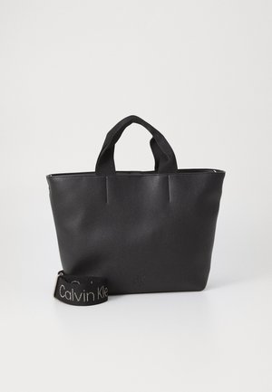 Borsa in pelle nera con manici superiori doppi, texture liscia e dettaglio del logo. Include una tracolla rimovibile con il marchio "Calvin Klein".