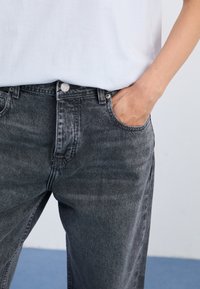 Grå denimjeans med en litt slitt finish, fem-lommers design, knappelukking og subtile sømdetaljer. Kombinert med en hvit skjorte.