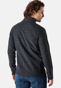 Dunkelgrauer, strukturierter Pullover mit hohem Kragen und langen Ärmeln, von hinten gezeigt, kombiniert mit blauen Jeans. Legere Passform und Design.