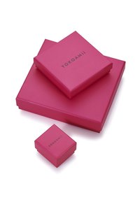 Trys kvadratiniai dovanų dėžutės ryškiai rožinės spalvos, su blizgiu paviršiumi. Didžiausioje yra juodu šriftu užrašyta "Yokoami" ant viršaus.