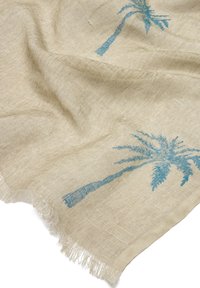 Beżowa tkanina o splocie, z frędzlami i niebieskimi wzorami palm, pokazująca teksturę i delikatne fałdy.