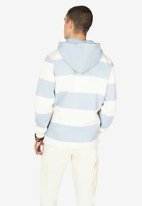 Hoodie in lichtblauw met witte strepen, voorzien van een kangoeroezak en geribbelde manchetten. De stof lijkt zacht en textuur te hebben.