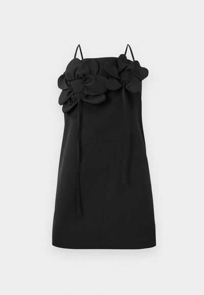 Fekete ruha vékony pántokkal, két nagy szövet virággal a dekoltázsnál. Simára csiszolt textúra és egyszerű, egyenes sziluett.