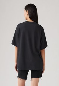 Sort oversize t-shirt lavet af bomuld, korte ærmer, rund hals, glat tekstur, båret med slidte sorte denimshorts.