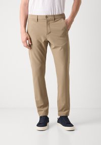 Pantaloni bej elastici cu un front plat, bucle pentru curea și buzunare laterale. Asortați cu pantofi bleu închis, cu o suprafață texturată și talpă albă.