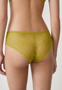 Slip verde in pizzo con motivo floreale, bordi ondulati e una trama semi-trasparente, progettato per una silhouette aderente.
