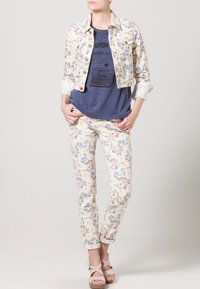 Džínová bunda s květinovým vzorem na světle krémovém pozadí, doplněná námořnicky modrým tričkem s potiskem, květinovými džínami a světle růžovými sandály na řemínky.