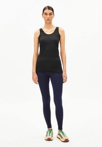 Zwarte tanktop, aansluitende en rekbare stof. Gecombineerd met marineblauwe leggings met een gladde textuur. Schoeisel: beige met groene en bruine accenten, sportief design.