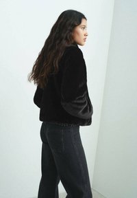 Chaqueta de piel sintética negra con mangas largas y diseño corto. Combinada con jeans de talle alto oscuros que presentan sutiles detalles de remaches en la cinturilla.