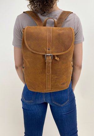 Brown leather backpack with a flap, buckle closure, and stitching details. Features padded straps and a top handle for carrying.