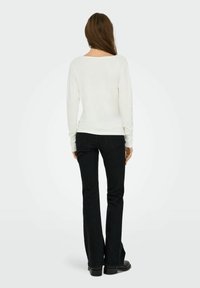Witte langemouwen top met een brede halslijn, gecombineerd met zwarte wijde jeans. De outfit heeft een gladde textuur en een aansluitend ontwerp.