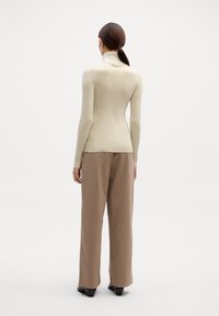 Bež prugast pulover s turtleneck ovratom v kombinaciji z bež širokimi hlačami, črnimi petkami in preprosto frizuro.