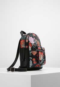 Szyta plecak florystyczny z czarną skórzaną bazą, okrągłym kształtem, podwójnymi suwakami i zewnętrzną kieszenią na zamek. Posiada żywe, wielokolorowe kwiaty.