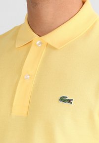 Żółta koszulka polo wykonana z fakturowanej tkaniny, z klasycznym kołnierzykiem, dwoma guzikami i haftowanym zielonym logo krokodyla.