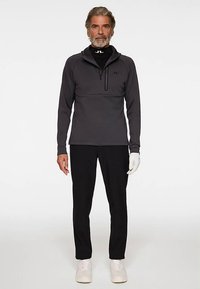 Maglione grigio a maniche lunghe con collo a mezza zip, abbinato a pantaloni neri e sneakers bianche. Presenta un dettaglio con logo e una vestibilità comoda.