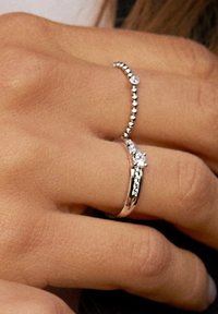 Zwei silberne Ringe an einer Hand; einer hat einen kleinen Diamantenakzent, der andere ein Perlenmuster. Glatte Oberfläche, glänzende Metalloberfläche.