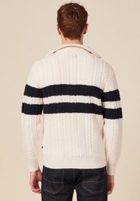 Cremfarbener Kabelstrickpullover mit marineblauen Streifen über der Brust und an den Ärmeln. Mit Kragen sowie gerippten Bündchen und Saum. Strukturierter Stoff.