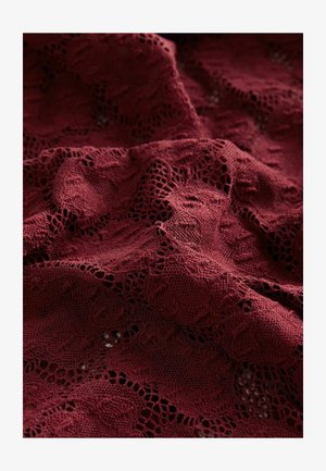Tessuto di pizzo bordeaux con un motivo floreale, caratterizzato da dettagli intricati e una leggera texture, drappeggiato in modo morbido per mostrare il suo fluire e la sua struttura.