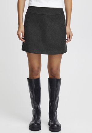 Mini-jupe en laine grise avec une taille ajustée, des détails de couture subtils, associée à des bottes en cuir noires jusqu'aux genoux.