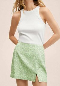 Un débardeur blanc à côtes associé à une mini-jupe verte à motifs floraux, avec une fente sur le côté et de petites fleurs blanches sur un fond vert clair.