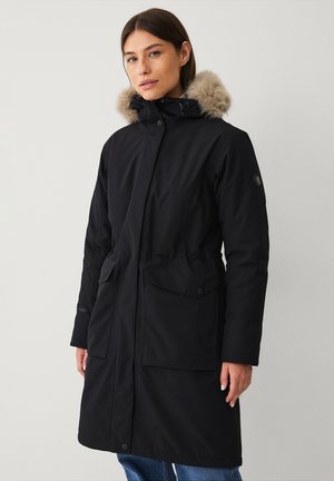 Lang sort parka-jakke med en pelsforet hætte, trykknapper, snoreliv og to forlommer. Fremstillet af et glat, holdbart materiale.