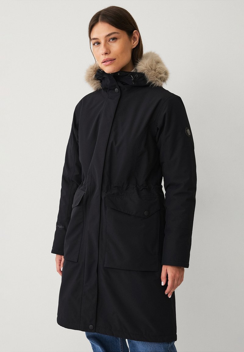 Lange zwarte parka jas met een met bont gevoerde capuchon, drukknoopsluiting, aantrekkoord in de taille en twee voorzakken. Gemaakt van een glad, duurzaam materiaal.