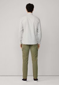 Camisa a cuadros de color claro para hombres con cuello abotonado, combinada con pantalones cargo verde oliva que cuentan con bolsillos laterales, vista desde la parte de atrás.