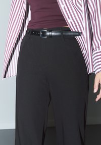 Svarta byxor med en slät textur, bärs med en vinröd topp och en rutiga skjorta med knappar som har vita och lila ränder.