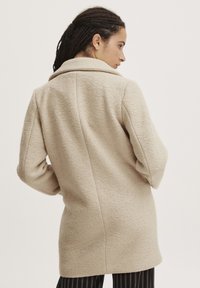 Beige gyapjúszál keverék kabát textúrált felülettel, kifordított gallérral és hosszú ujjakkal, tiszta, testre szabott sziluettel.