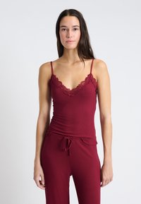 Vinröd ribbad linne med spetkanter och tunna axelband, med en figurnära design och en lätt utsvängning vid fållen, tillsammans med matchande byxor.