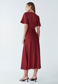 Burgundska midi obleka s kratkimi rokavi, gladko teksturo, prilegajočim pasom in razširjenim krilom. Ima zadrgo na hrbtni strani.