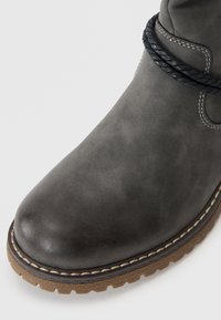Botte en cuir gris à bout arrondi, ornée d'un accent de corde noire et de surpiqûres blanches contrastantes sur une semelle brune texturée.