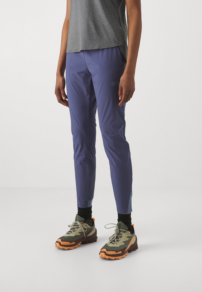 Paarse lichtgewicht broek met taps toelopend ontwerp, voorzien van zijzakken en contrasterende blauwe accenten aan de randen. Draagt met chunky sneakers.