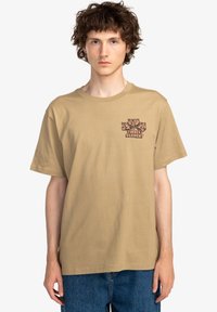 Tan short-sleeve t-shirt featuring a colorful graphic of bears and text "TIMBER ELEMENT" on the left chest. Cotton material, relaxed fit.
