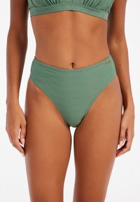 Žalios spalvos aukštai įsiūti bikini apatiniai su tekstūruotu geometriniu raštu, lygiu audiniu ir maženiu aukso logotipo akcentu šone.