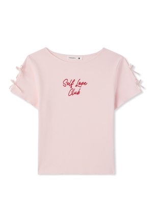 Maglietta rosa chiaro a maniche corte con motivo a costine, testo rosso "Self Love Club" centrato e piccoli fiocchi legati su ogni manica.