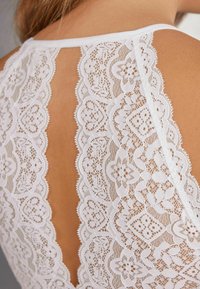 Blus i spets med ett detaljerat blommönster, vit färg, med skopa-bakdesign och vågiga kanter. Mjuk textur med intrikata detaljer.