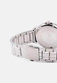Reloj de acero inoxidable plateado con pulsera de eslabones, que presenta una caja redondeada, un cierre sencillo y un acabado metálico suave en la parte posterior del reloj.